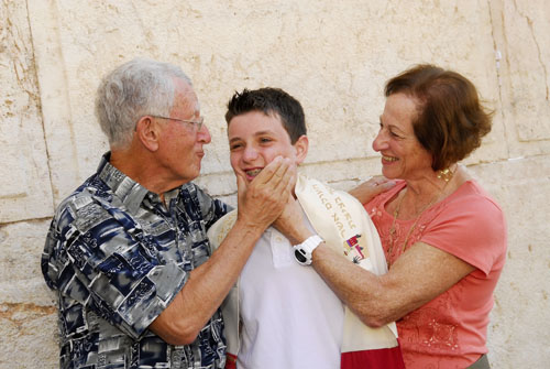 Grandparents warmly holding their grandson after wrapping him in his tallit